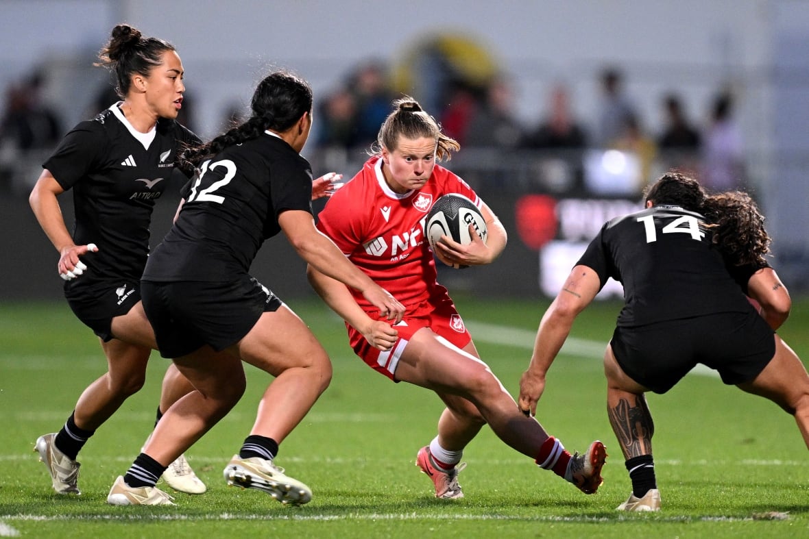 A women's rugby player in an all red uniform tries to evade tackles from three other women's rugby players wearing all black.