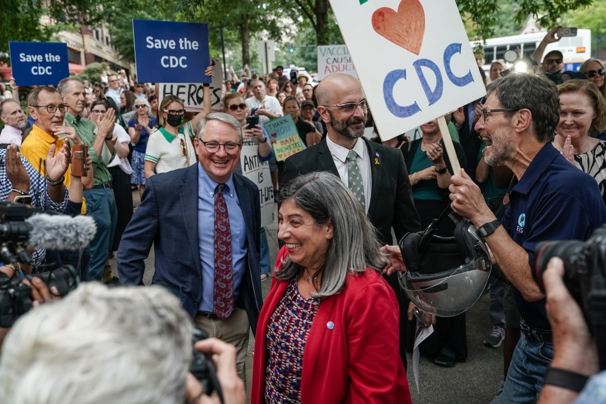 Several people are shown, men and women, at an outdoor demonstration with signs behind them.