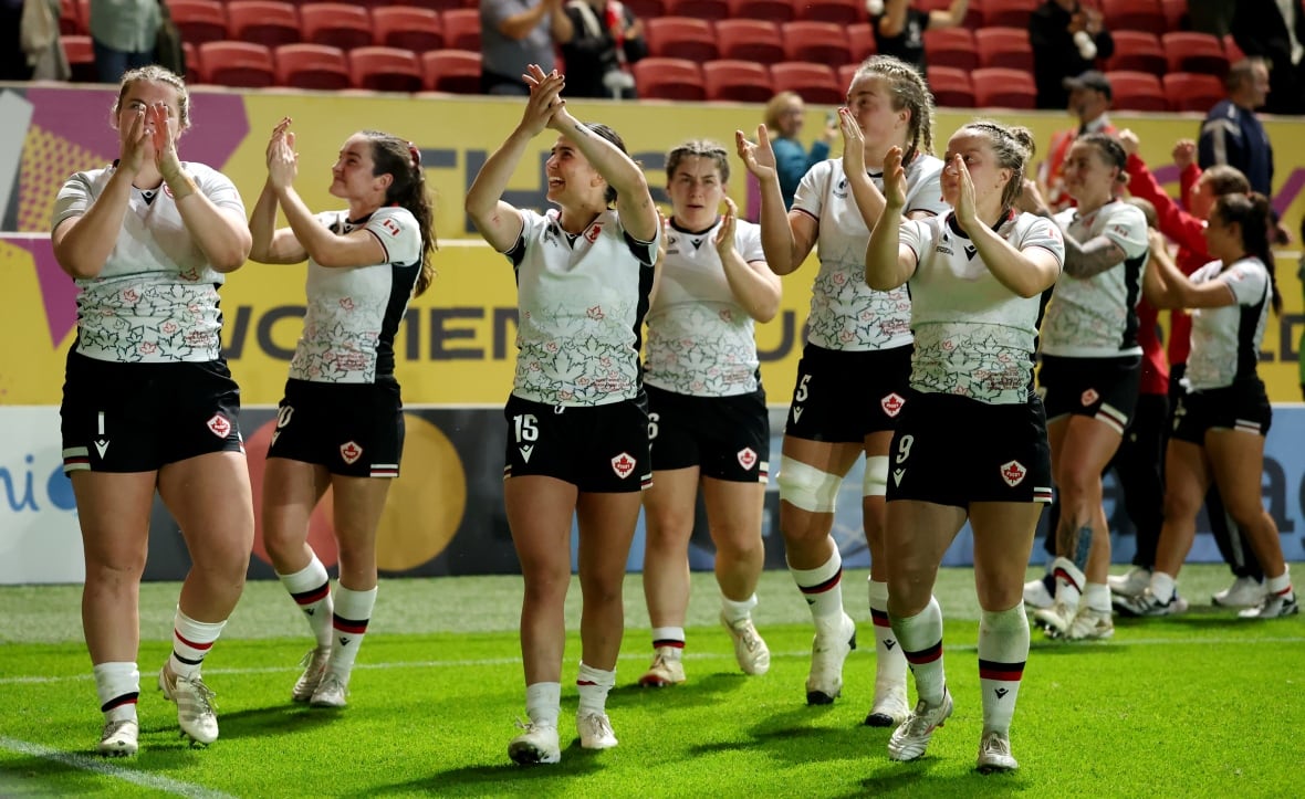 Women's rugby players clap toward the crowd.
