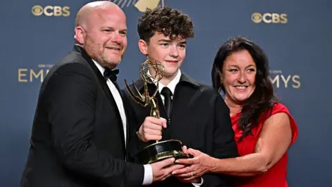 Getty Images British actor Owen Cooper (C) poses in the press room with the award for Outstanding Supporting Actor in a Limited or Anthology Series or Movie for "Adolescence", alongside his parents Noreen (R) and Andy Cooper (L) during the 77th Primetime Emmy Awards at the Peacock Theatre at LA Live in Los Angeles on September 14, 2025.