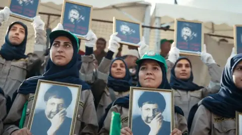 Women in green caps, darks scarves and khaki uniforms hold framed photos of Musa al-Sadr in a demonstration on the anniversary of his disappearance last year