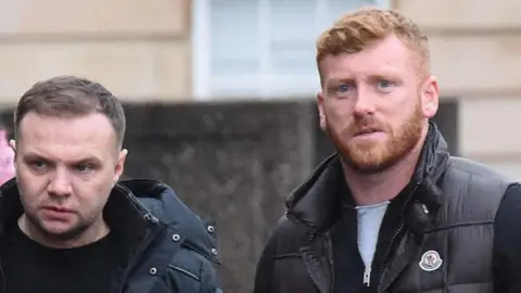 Spindrift Eddie Lyons, left, who has short, dark hair and is looking slightly off camera. He is wearing a dark jacket over a dark t-shirt. Ross Monaghan, right, is looking straight at the camera. He has ginger hair and a ginger beard and is wearing a dark gilet over another dark top.