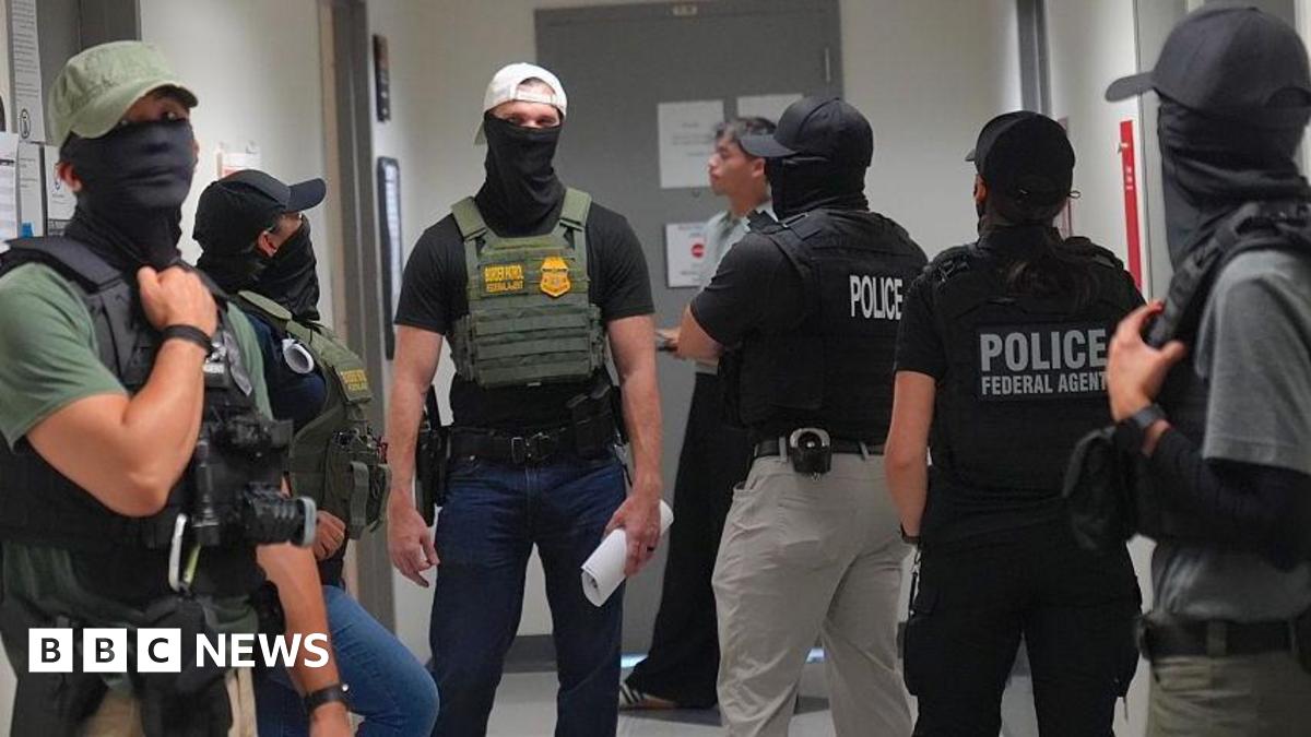 Immigration and Customs Enforcement (ICE) agents wear masks and stand in a corridor