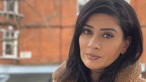 Sophia K Choudry Sophia Choudry in front of a red brick building wearing a sandy-coloured warm bobbly jacket