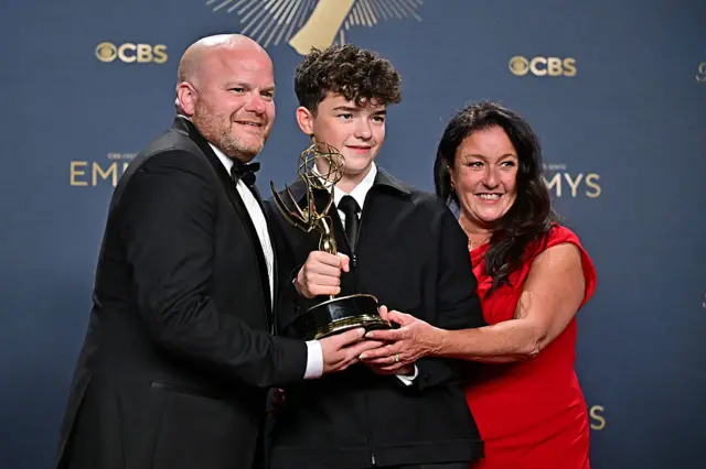 British actor Owen Cooper (C) poses in the press room with the award for Outstanding Supporting Actor in a Limited or Anthology Series or Movie for "Adolescence", alongside his parents Noreen (R) and Andy Cooper (L)
