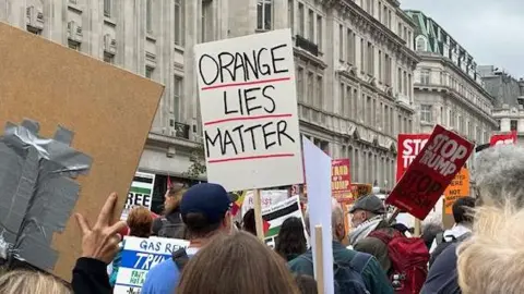 White placard with handwritten sign Orange lives matter in black ink, and underlined with red. person holding it is a crowd with lots of other people