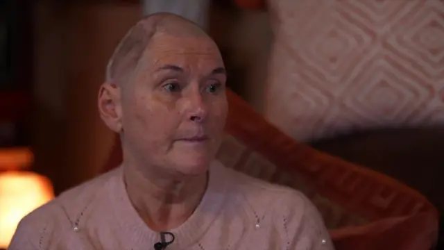 Woman wearing pink jumper stares off to the right side of the camera.