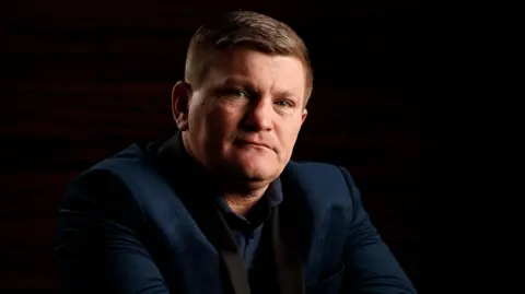 PA Media Ricky Hatton, dressed in a navy jacket, and shirt. He has short dark hair and is looking into the camera.