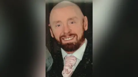Police Scotland James Clacher, a bald man, with a dark beard smiling while wearing a suit and pink tie.