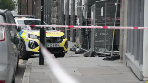 BBC A police car outside at the Thistle City Barbican Hotel. The area is surrounded by police tape