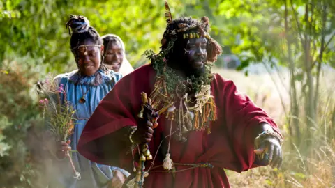 PA Media The three members of the tribe walk through the forest, with Kofi Offeh at the front.