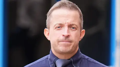 PA Media Haden Pentecost wearing a navy blue shirt and tie, looks at the camera