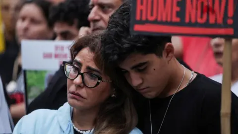 Getty Images A teenage boy wearing a black t-shirt leans his head against an older woman  wearing a pale blue top among a crowd of people.