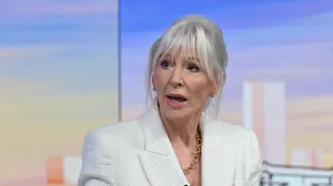 BBC Nadine Dorries wearing a white suit and sitting in a TV studio 