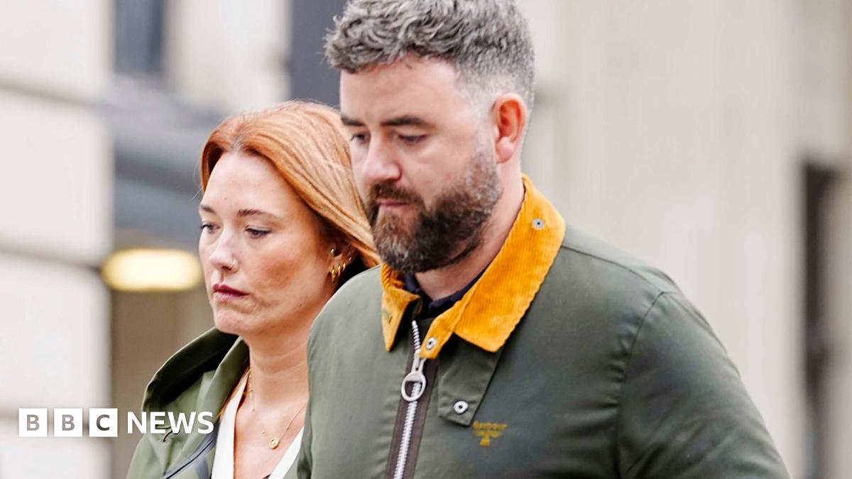 Lauren King, who has long red hair and is wearing a green coat, walks arm-in-arm with Ben King, who has dark hair peppered with grey and a brown beard. They both look sombre.