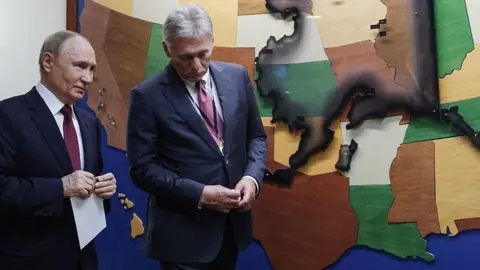 GAVRIIL GRIGOROV/POOL/AFP Two men in suits stand with a backdrop showing American states including Alaska.