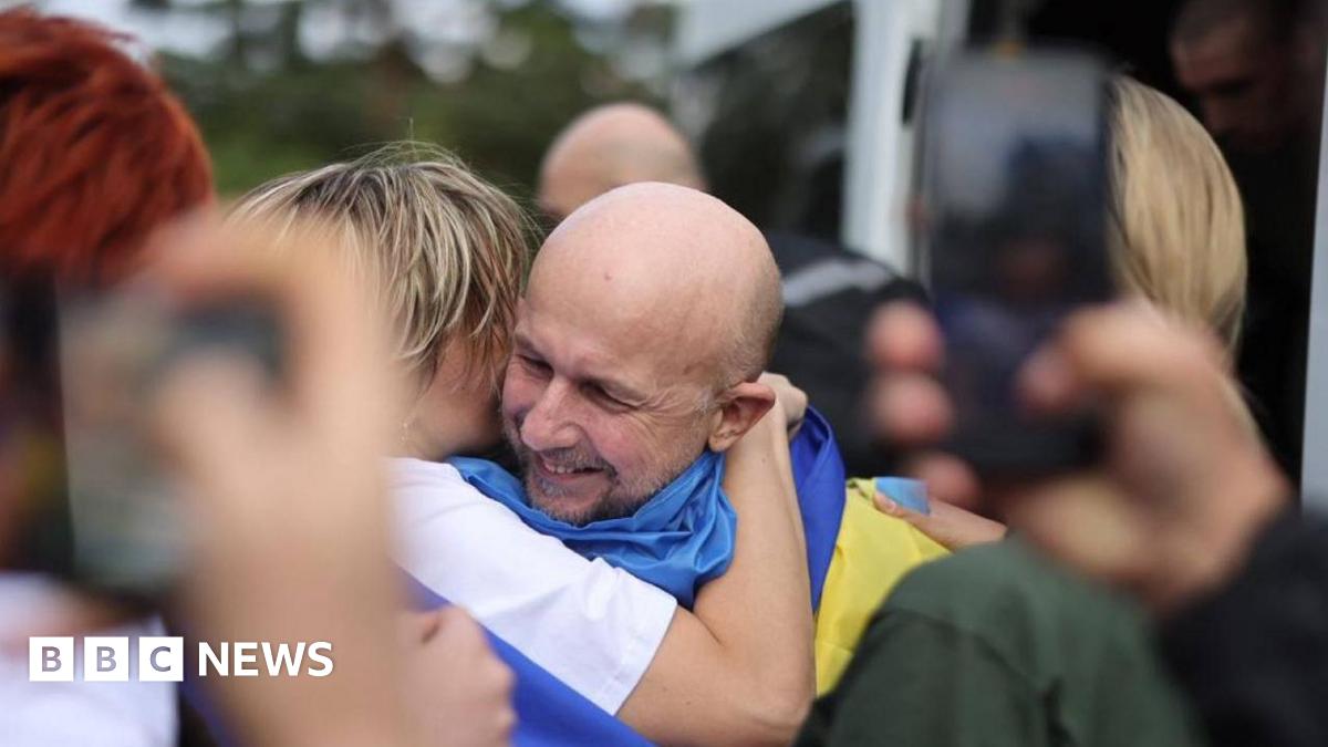 Dmytro Khyliuk stands looking into the camera, wearing a yellow shirt and headphones