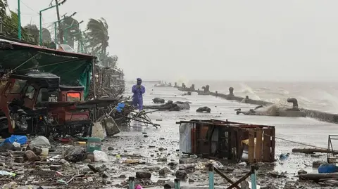 Getty Images A man stands near debris on a waterfront road due to heavy rain from Super Typhoon Ragasa in Aparri town in the Philippines