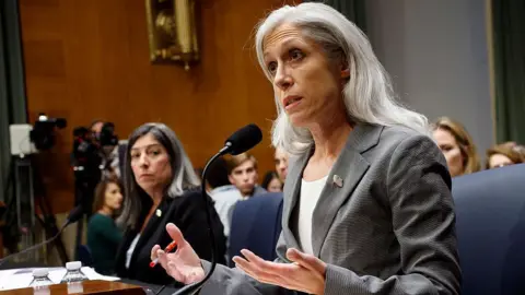 Getty Images Former Centers for Disease Control (CDC) Chief Medical Officer Dr. Debra Houry and former Director of the Centers for Disease Control (CDC) Susan Monarez testify before the Senate Committee on Health, Education, Labor, and Pensions in the Dirksen Senate Office Building on September 17, 2025 in Washington, DC.
Monarez is speaking animatedly with her hands into a microphone. She has shoulder length silver hair, and is wearing a grey suit jacket with a white scoop-neck top underneath. To her left is Debra Houry, who has white and black shoulder length hair, and is wearing a black suit jacket with a white blouse underneath. Behind them are seated spectators. 