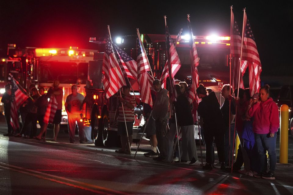 Community members held American flags and saluted as police and emergency vehicles formed a procession to the coroner’s office (Matt Slocum/AP)