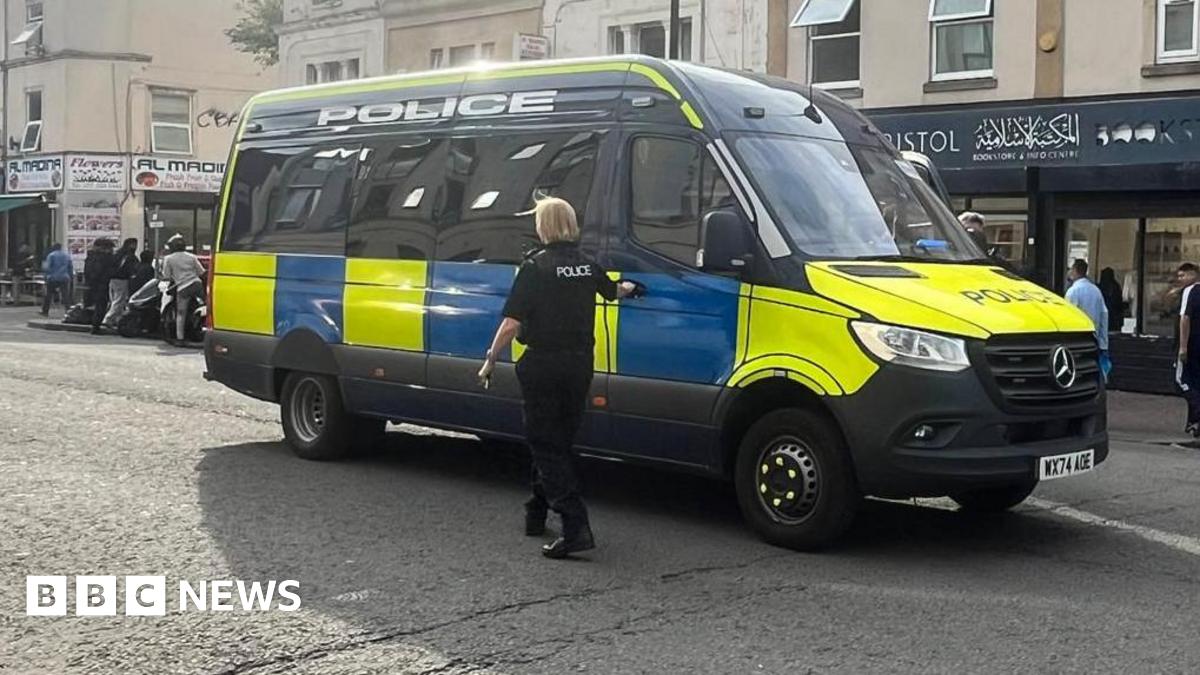 A police van on a closed road. A police officer stands outside it.