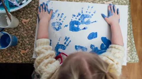Getty Images A bird's eye view of a young girl wearing a cream sweater making handprints on a page with blue paint