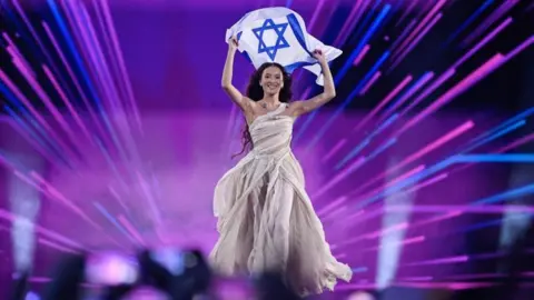 EPA Eden Golan representing Israel holds the flag of Israel on stage at the Eurovision Song Contest in 2024