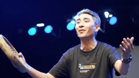 BBC Shohruhmirzo Ganiyev singing on stage with a drum