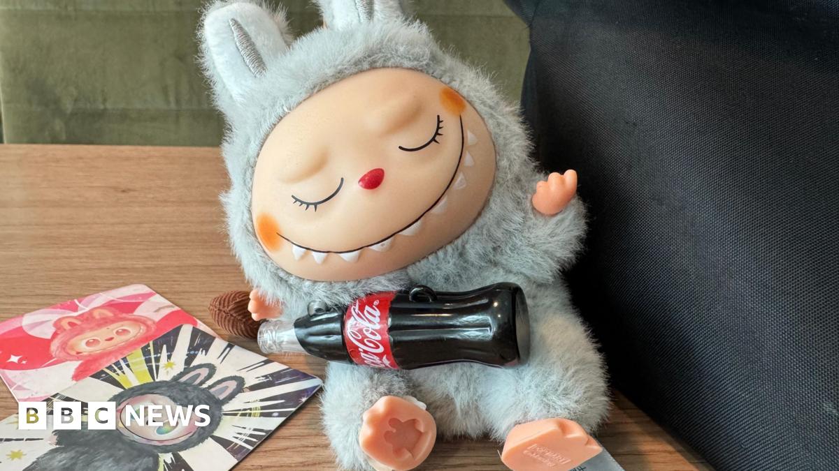 A fake grey Labubu with badly drawn smile and a hole in its foot is pictured next to official Labubu identity cards