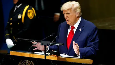Chip Somodevilla/Getty Images President Donald Trump wearing a blue jacket and red tie gestures with his hands as he stands at a lectern during the 80th session of the UN’s General Assembly (UNGA) at the United Nations headquarters on September 23, 2025 