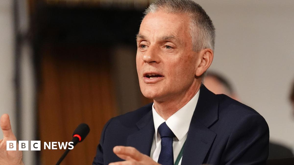 Tim Davie wearing a navy blue suit, navy tie and white shirt