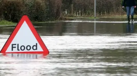 PA Media Library image of a flood sign, partly submerged in water on a flooded road.