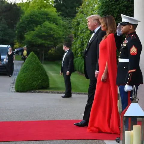 MANDEL NGAN/AFP via Getty Images Donald and Melania Trump - in dinner attire - stand on a red carpet awaiting arrivals as a soldier salutes next to them 