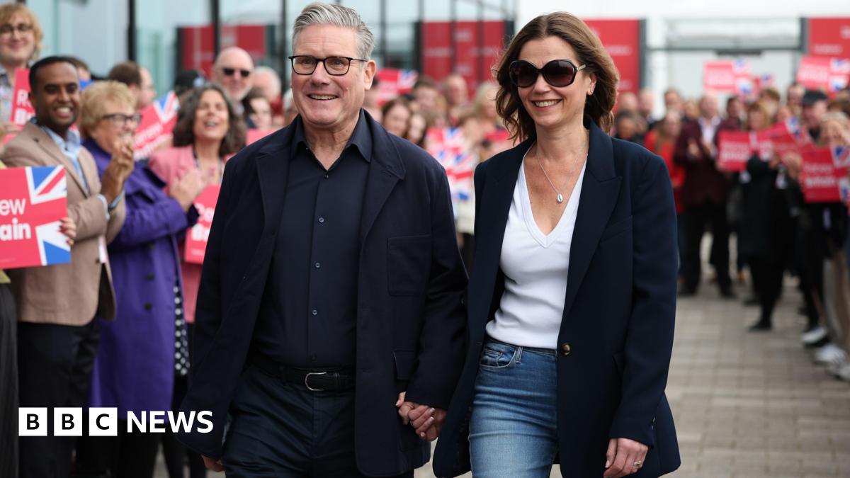 British Prime Minister Sir Keir Starmer and his wife Victoria arrive on the eve of the Labour Party Conference in Liverpool. He wears a dark jacket, shirt and trousers and holds her hand. Victoria wears a navy blue coat, jeans, shades and a white top.