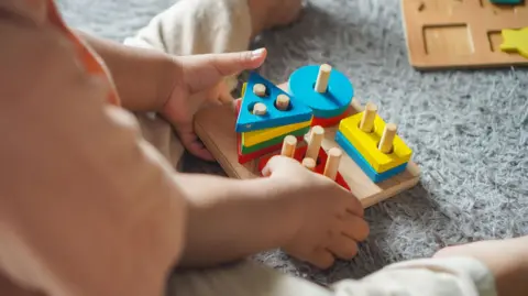 Getty Images A baby plays with colourful puzzles. Wooden blocks in squares, circles and triangles are placed onto pegs in a simple toy.