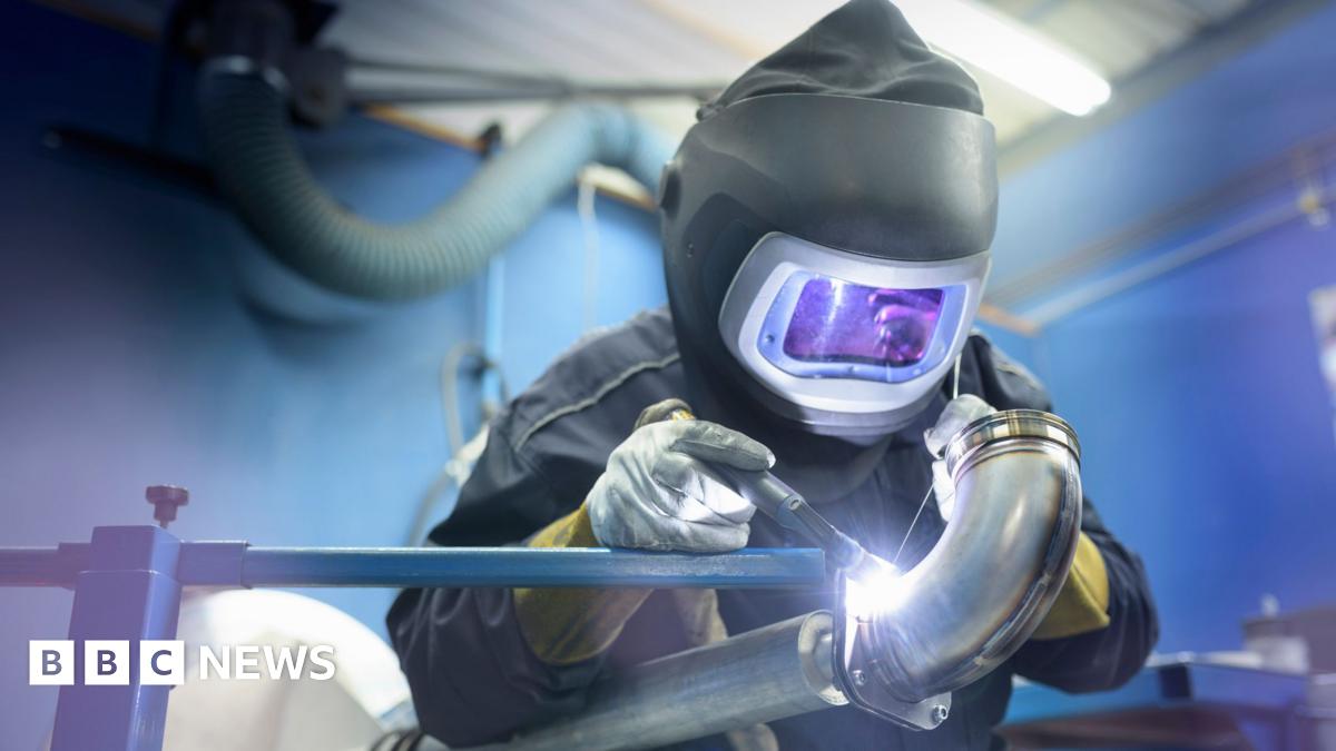A welder in protective clothing is welding a pipe
