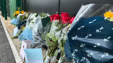 George Carden/BBC A number of floral and card tributes left for the late Billy Vigar at Chichester City football club. Six separate floral tributes can be seen in a row alongside three cards. 