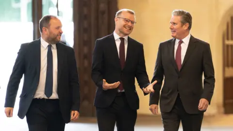 PA Media Murray, shanks and starmer walk along a corridor in a row wearing dark suits and ties.
