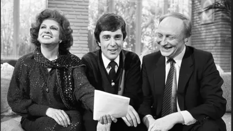 PA Media Former Coronation Street star Pat Phoenix laughs alongside John Stapleton and Labour leader Neil Kinnock in a TV studio