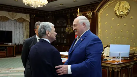 EPA/ Shutterstock A big man in a blue jacket grips a smaller man by the arm on the left