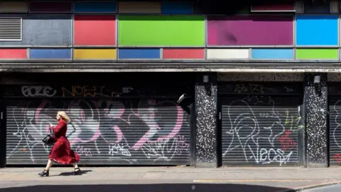 Getty Images A woman walks past two shops with the shutters closed.