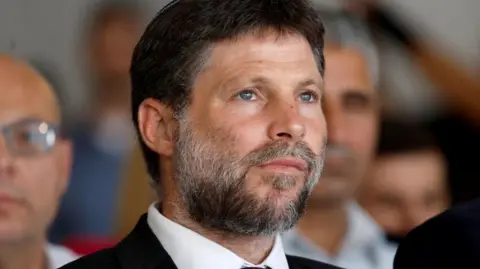 Reuters A close-up photo of a man with a beard wearing a suit. He is looking to the right of the camera, and there are other men in the background, their faces out of focus