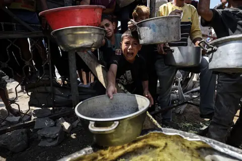 Getty Images A child wails as he and others hold empty pans towards the camera