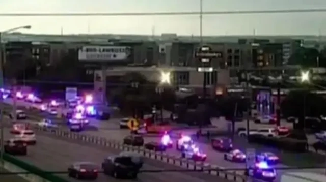 A wide view of a street in which multiple police cars with flashing lights are parked