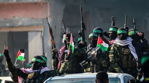 Getty Images A number of armed Hamas militants arrive in an area before releasing Israeli hostage Agam Berger to a Red Cross team in Jabalia, Gaza on 30 January 2025, as part of a hostage-prisoner exchange. The fighters wear black sunglasses, black balaclavas, green headbands and keffiyeh scarves. Most of them carry guns and three are also waving Palestinian flags. 