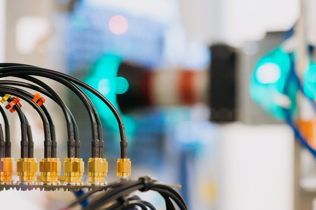 A close-up image of a curved line of cables attached to a metal plate, with bright lights of different colors glowing in the background.