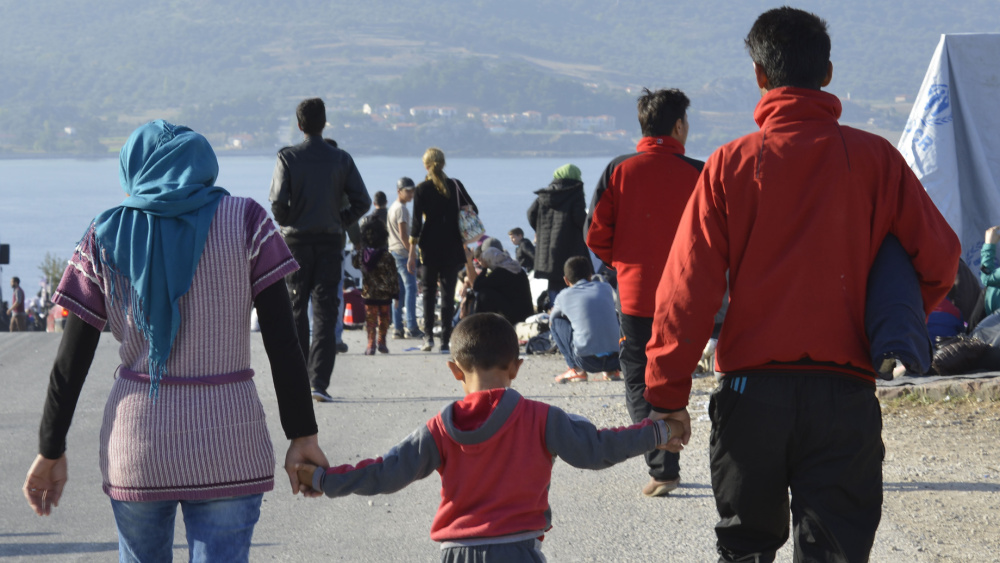 A man and a women walking through a refugee camp with a child between them holding their hands.