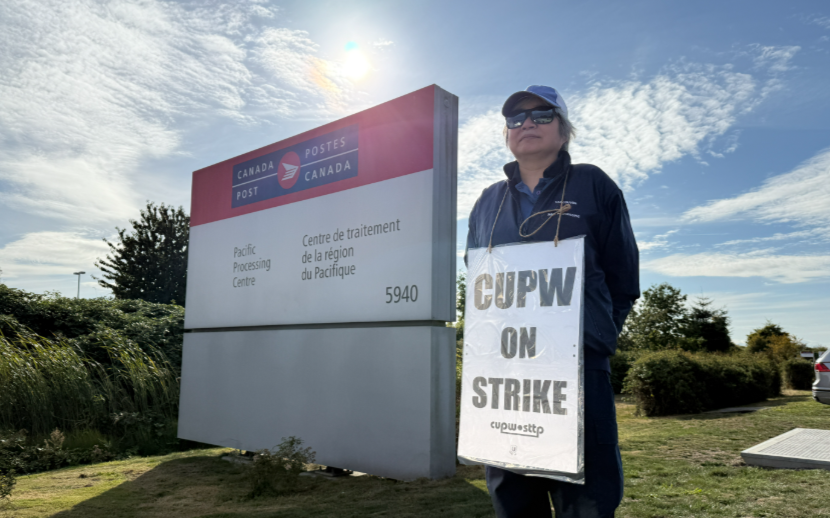 A picketer stands outside Canada Post's Pacific Processing Centre in Richmond, B.C., on Sept. 25, 2025.