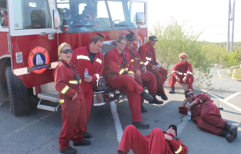 A group of people in red uniforms stand in a parking lot near a fire truck.