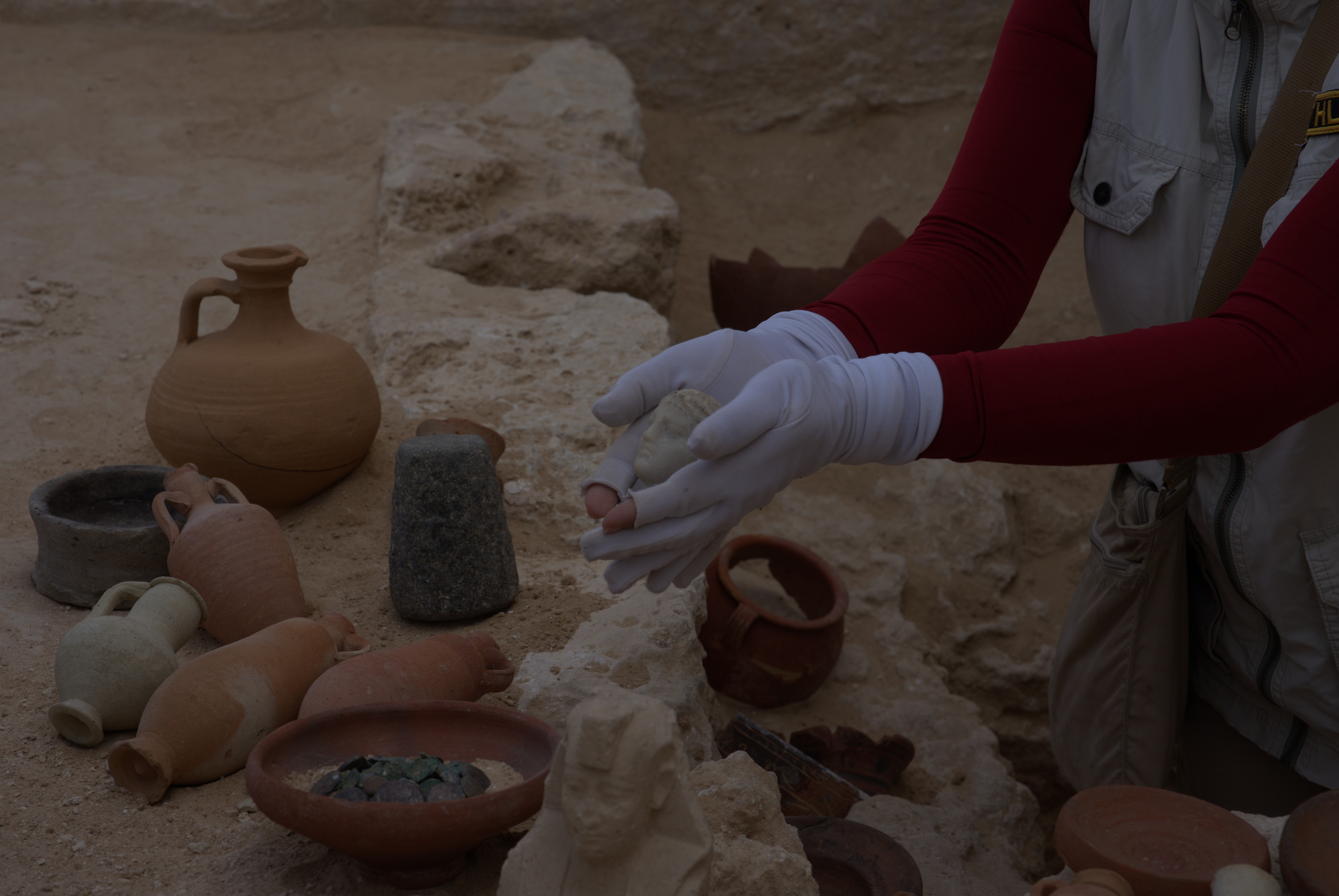A woman holds a small marble bust in her hands near other artifacts &mdash; ceramic bowls and coins.